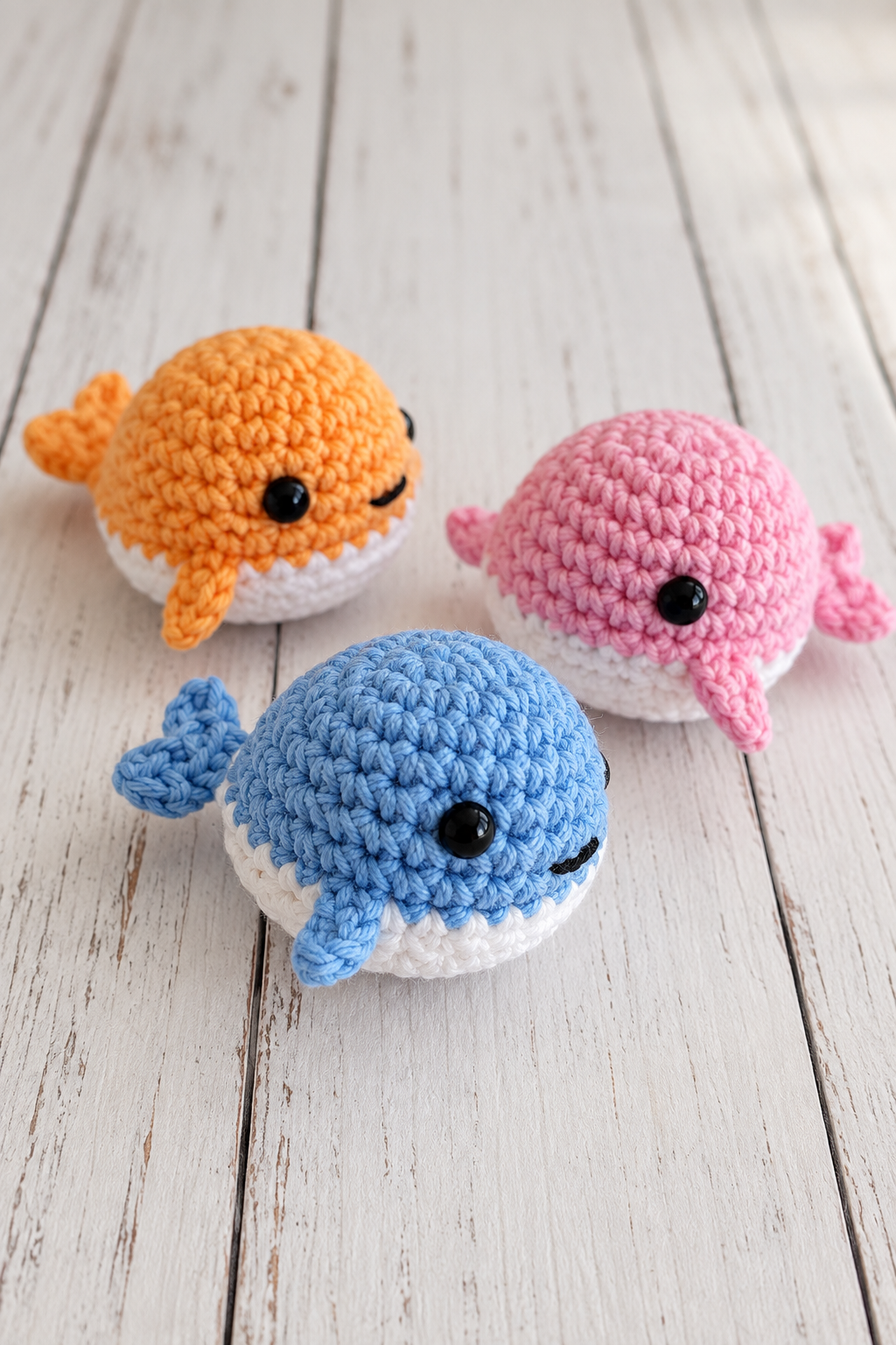 Tiny pastel crochet whales arranged on a light craft surface